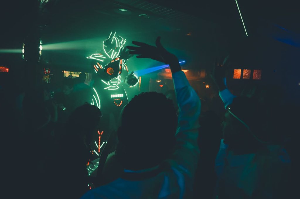 Unrecognizable person in futuristic costume with neon lights making show in dark nightclub near dancing people
