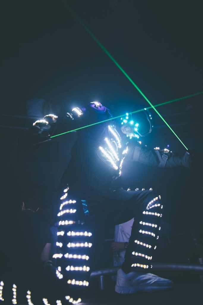 Energetic dancer in illuminated suit creating vibrant neon light trails indoors at night.
